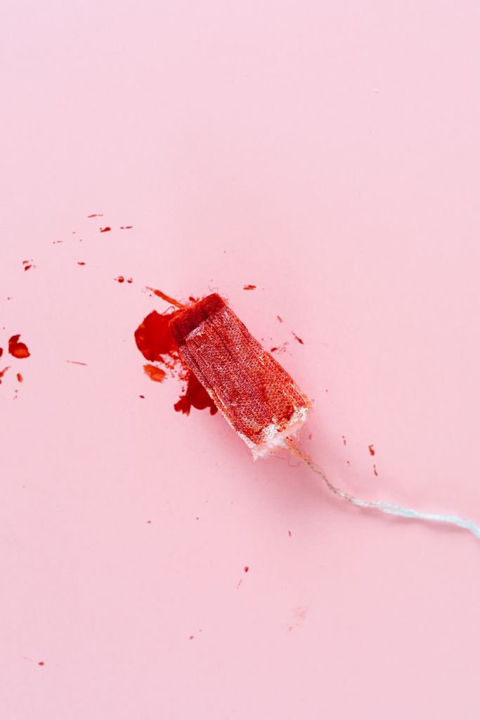 A high-angle view of a tampon with red stains on a soft pink background, symbolizing menstruation.